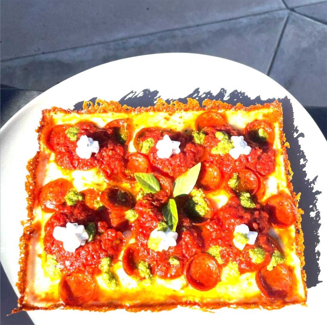 An overhead shot of a Detroit-style square pizza with bright red sauce dollops, pepperoni and pesto.