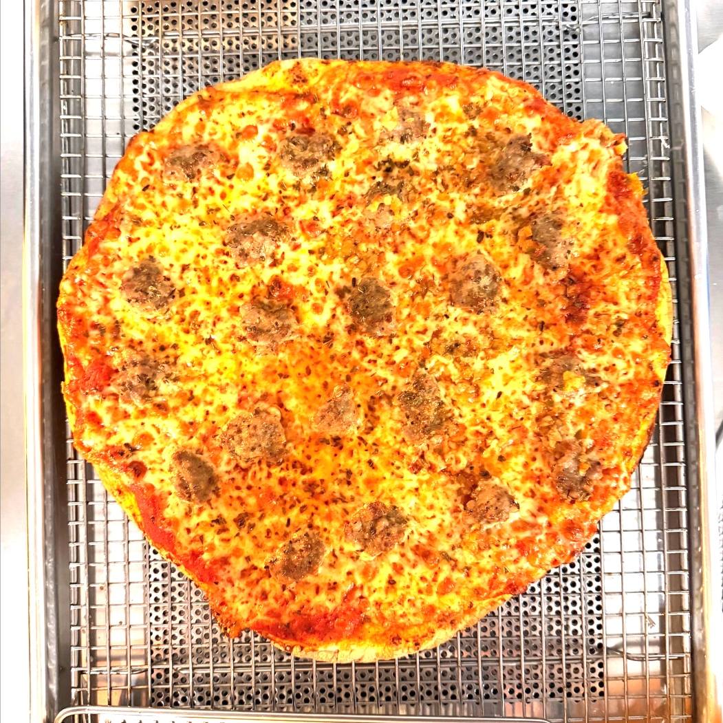 A whole tavern-style pizza with sausage crumbles on a wire baking rack — thin crust, edge-to-edge cheese.