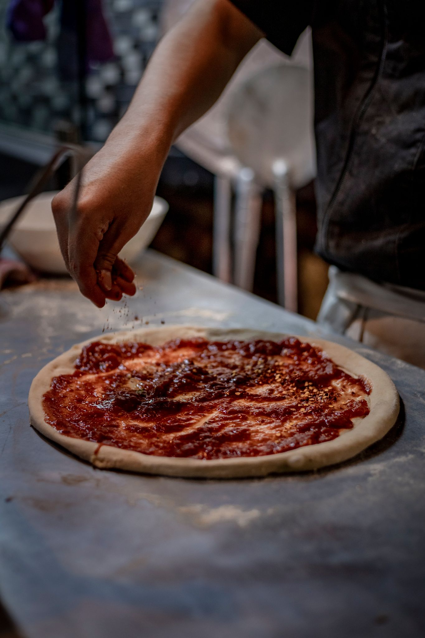 Close-up of a person seasoning pizza dough with sauce, capturing the art of cooking.